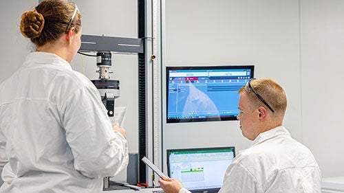 Two workers in lab coats view a computer screen together