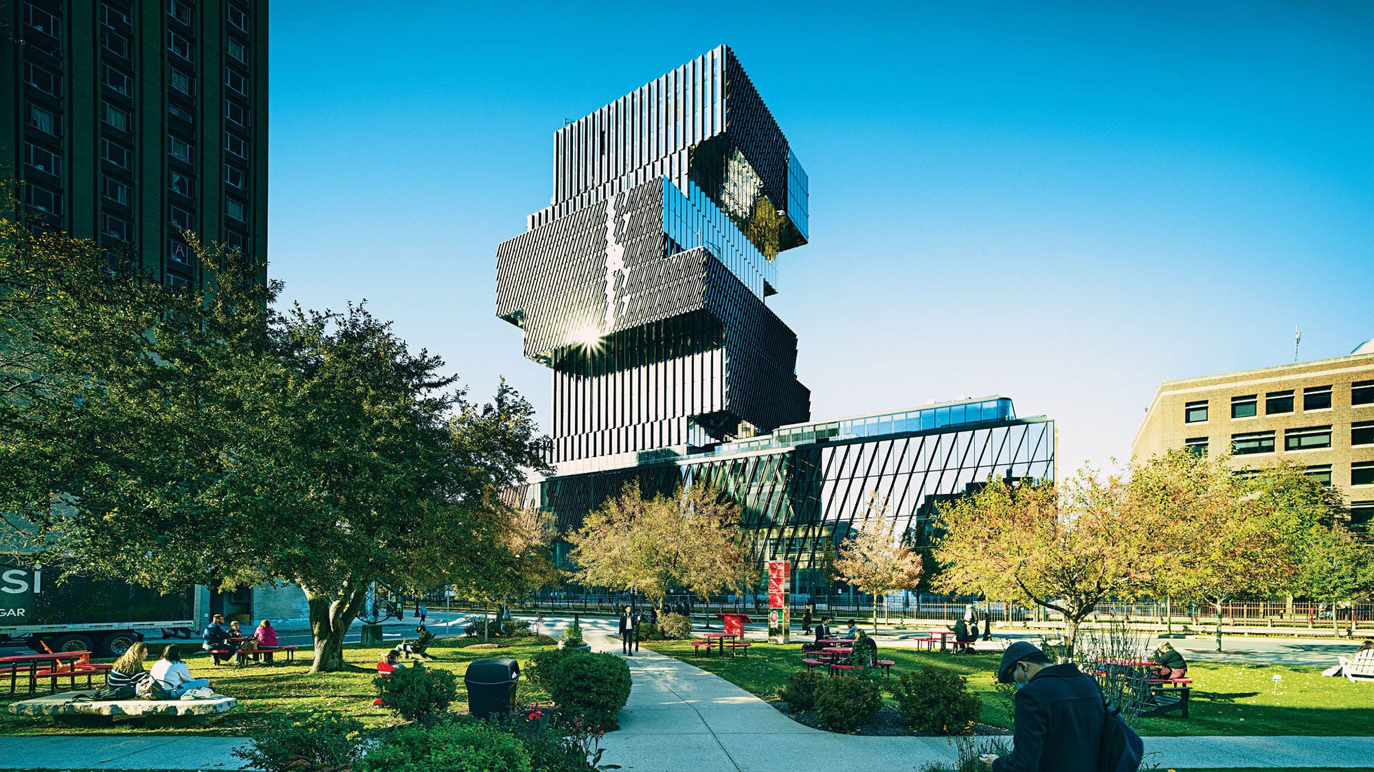 A large, tall tower made up of rectangular blocks rises behind a green city park