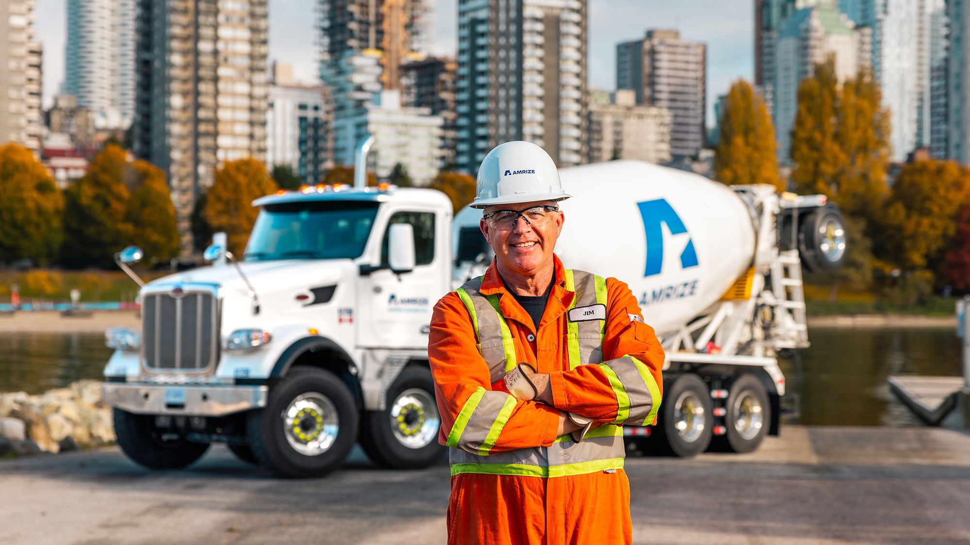Amrize RMX truck against a cityscape background featuring an Amrize truck driver front and center garnering Amrize personal protective equipment.  