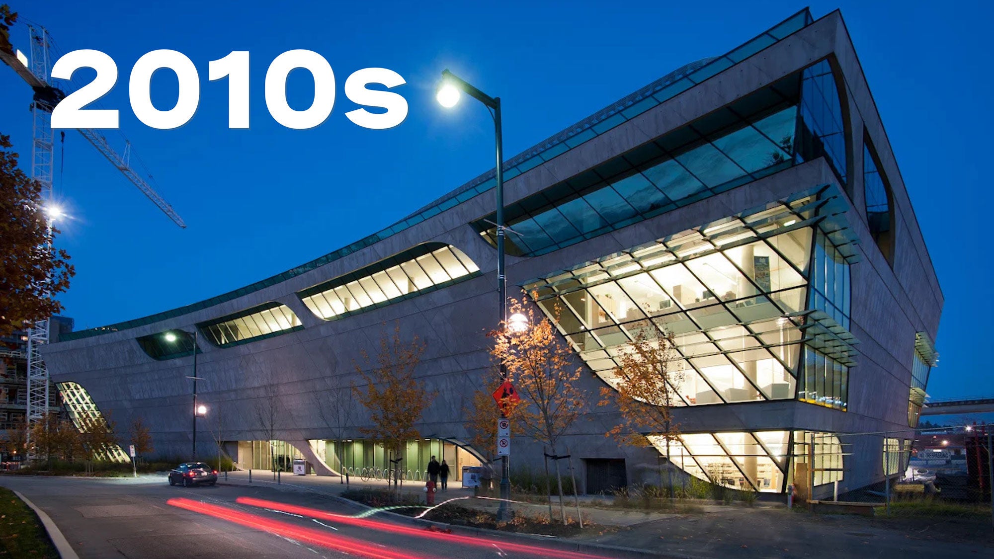 An image of a building at dusk with lights shining through its large windows and a clear, darkening sky behind.
