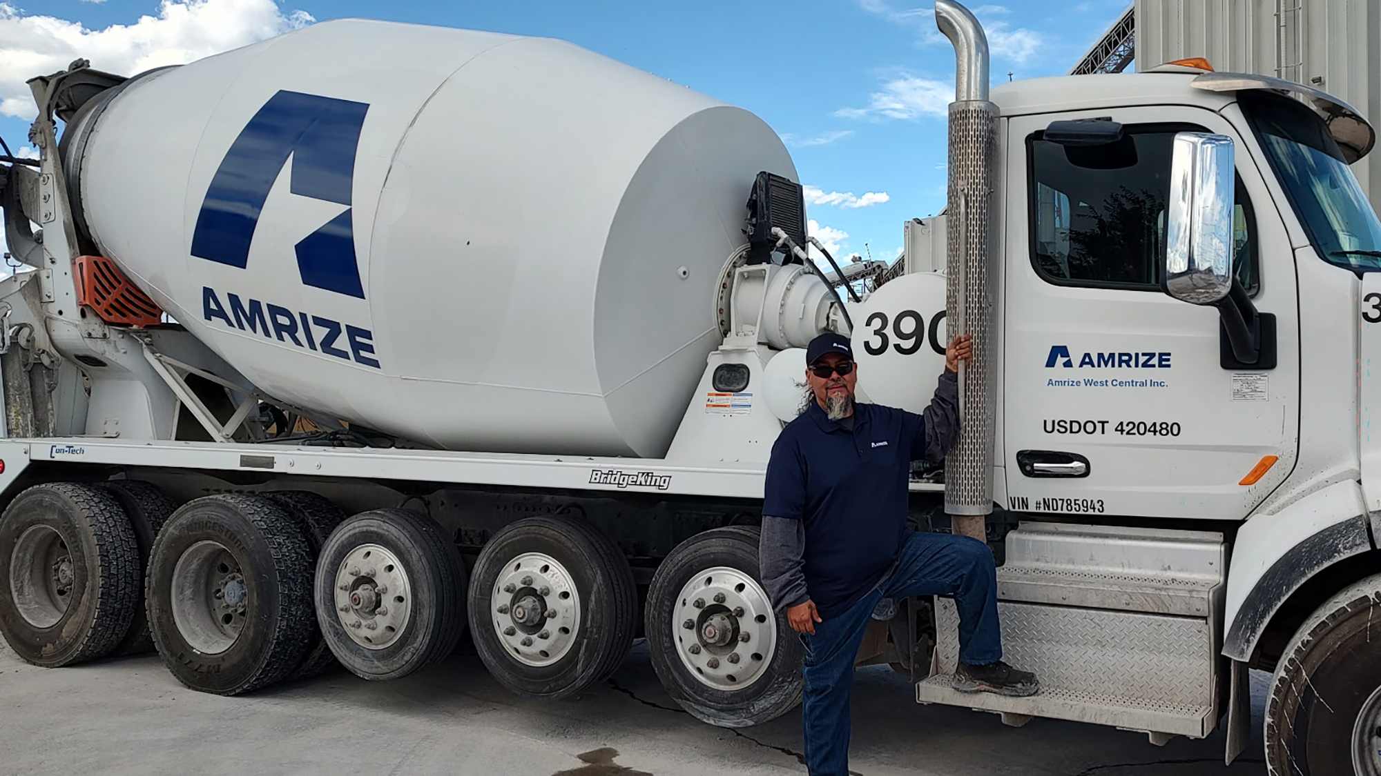 A close up image of a white RMX truck with Amrize logo displayed across in blue featuring a driver stepping up to enter the driver seat. 