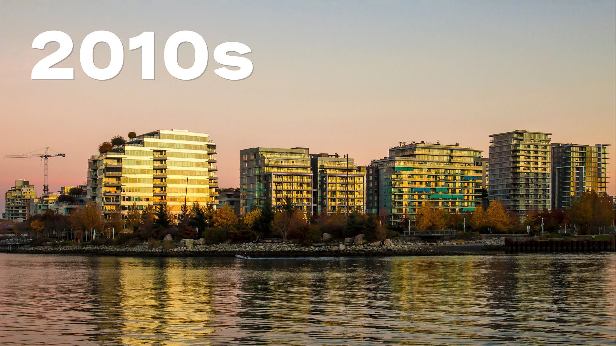 Sunset view of a cityscape with modern high-rise buildings reflecting warm light across a calm river. The sky is a soft gradient of pink to blue. The word “2010s” is in bold white text above. 
