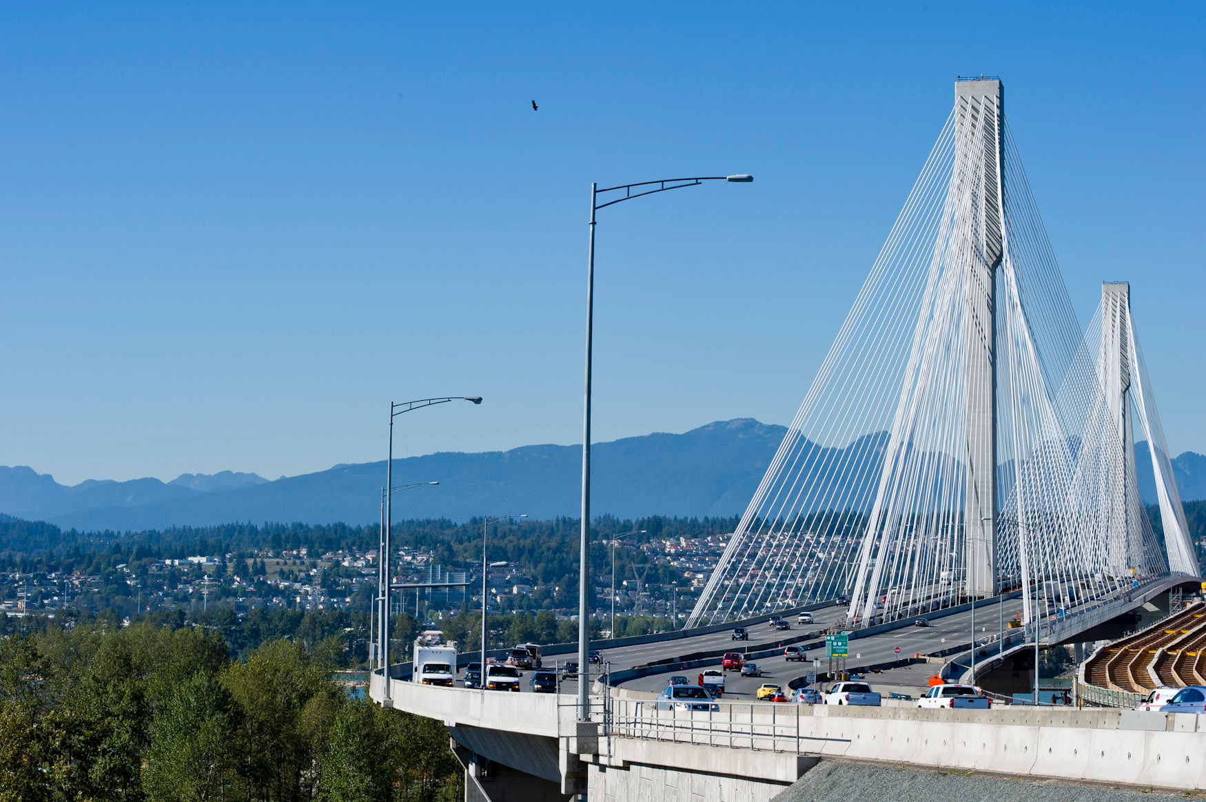 Un grand pont avec une tour centrale s’étendant au-dessus d’une rivière invisible vers les montagnes au loin.