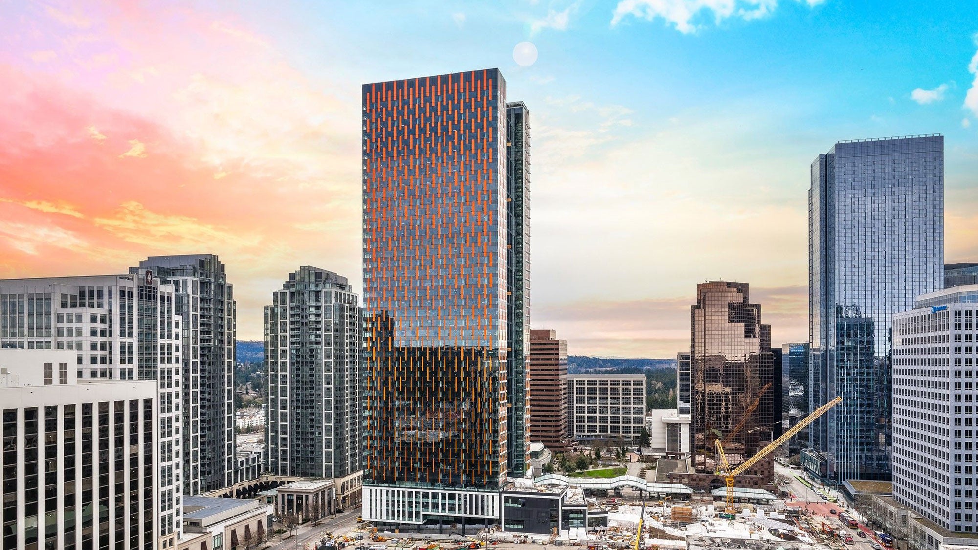 A large, modern skyscraper risers from a downtown setting at dawn