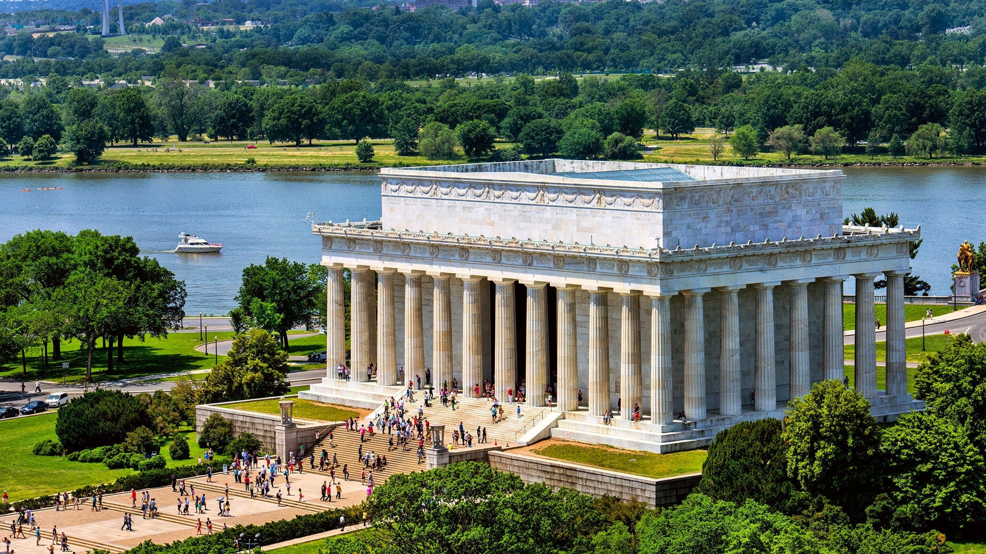A large, white, columned monument sites amid a park in front of a blue river