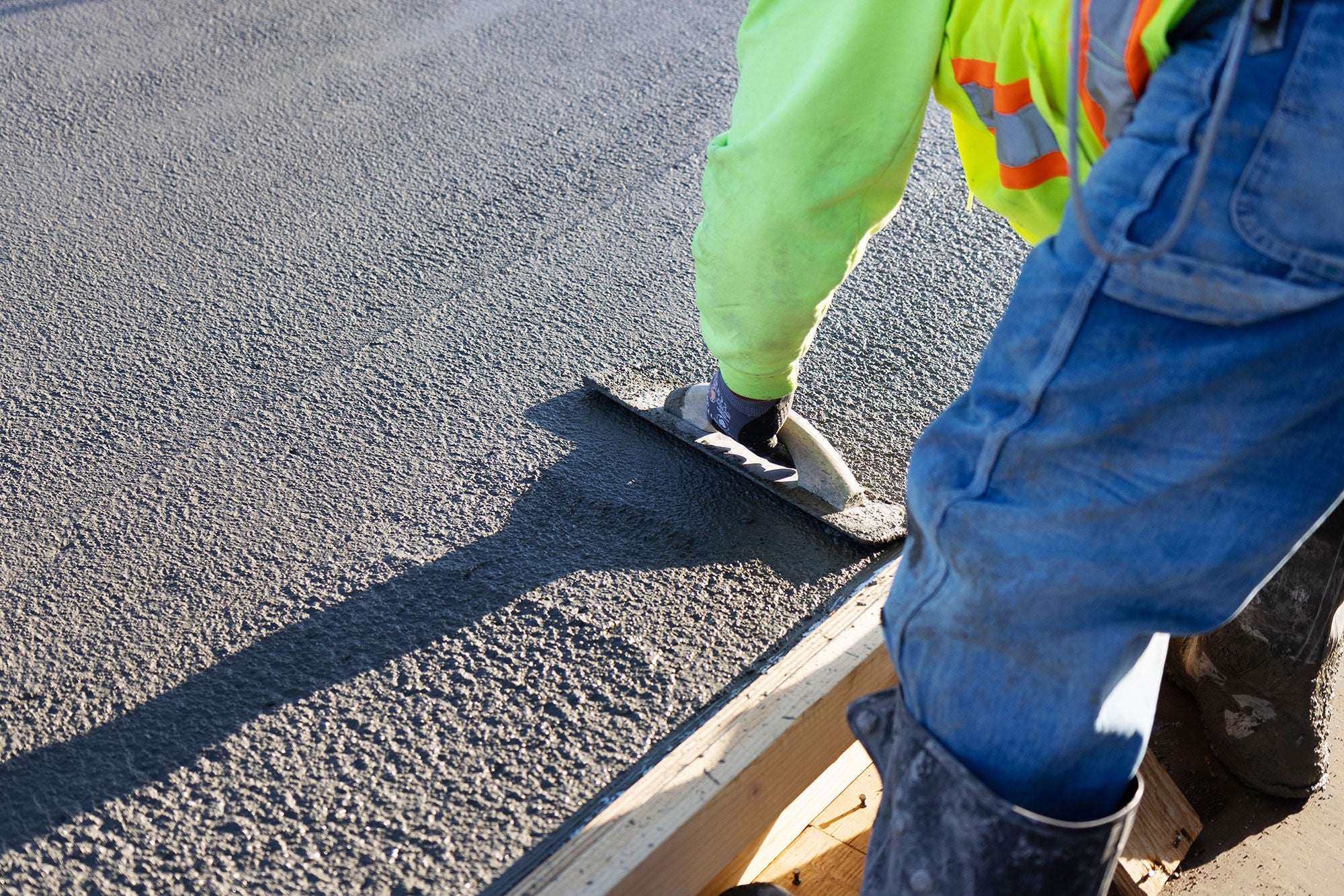 A view from behind as a person bends over to smooth concrete that has not set yet