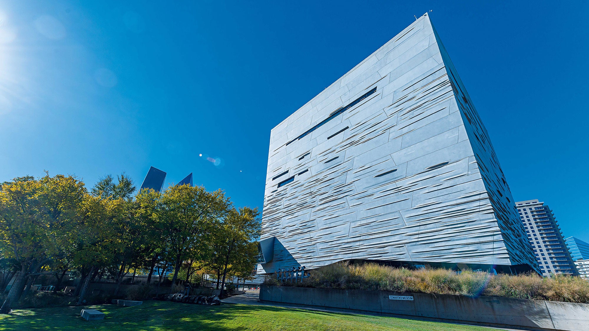 The facade of a large concrete tower rises above a city park into a blue sky