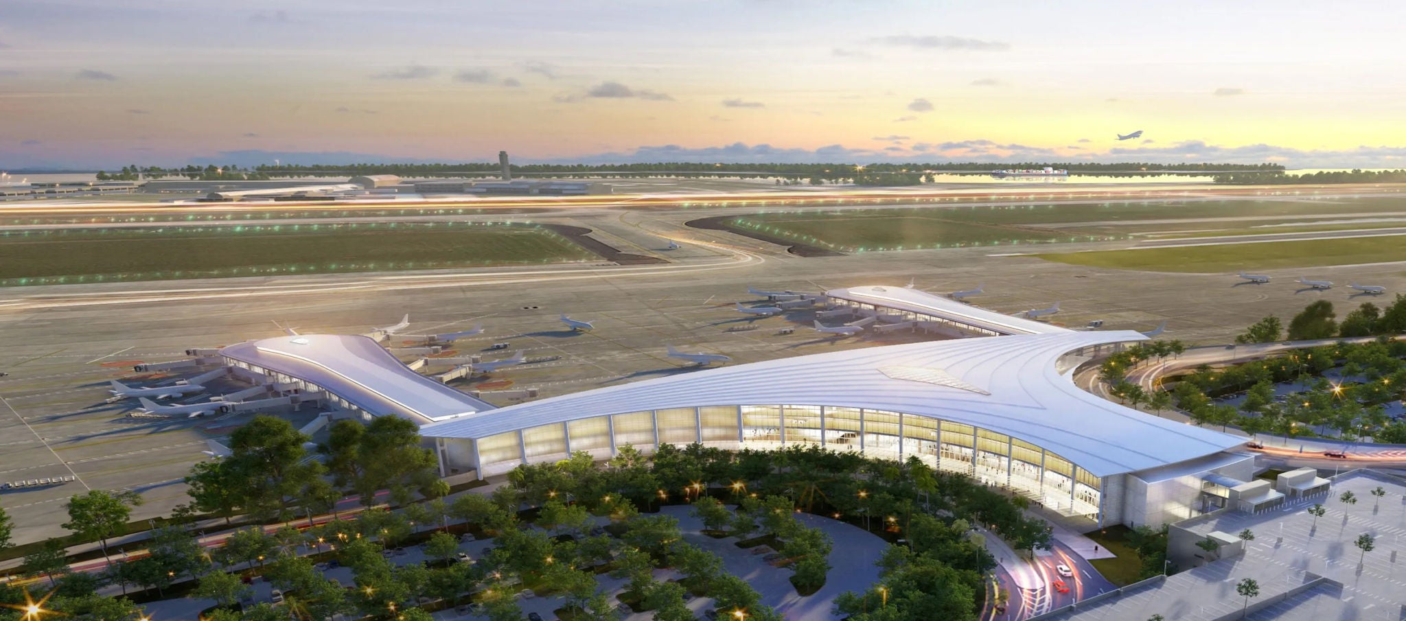 An aerial view of a large airport terminal in front of a set of runways at dusk