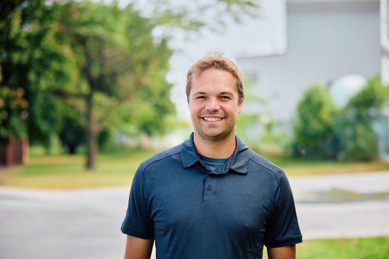 Un homme qui sourit à la caméra devant un arrière-plan résidentiel flou
