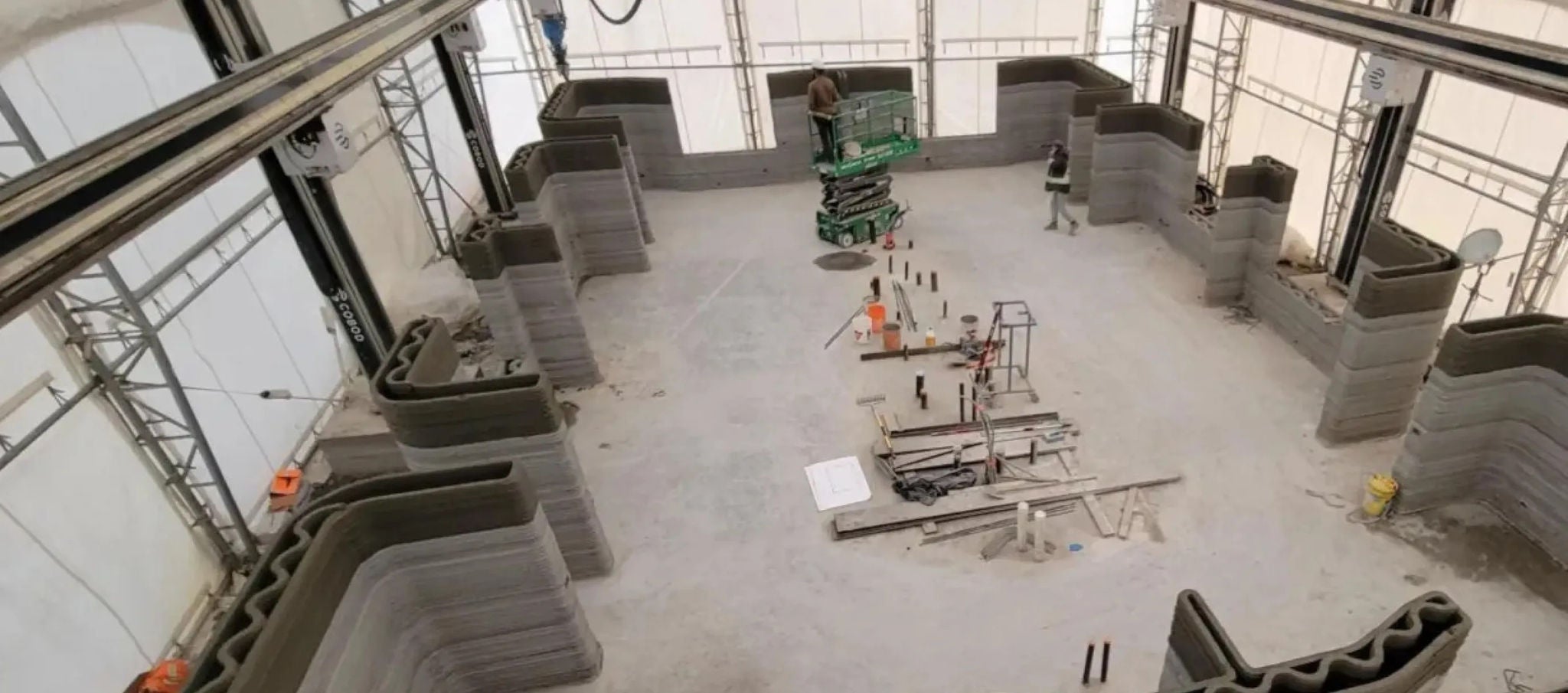 Une vue aérienne d’un chantier de construction imprimé en 3D avec des murs incurvés et des ouvriers utilisant des machines.