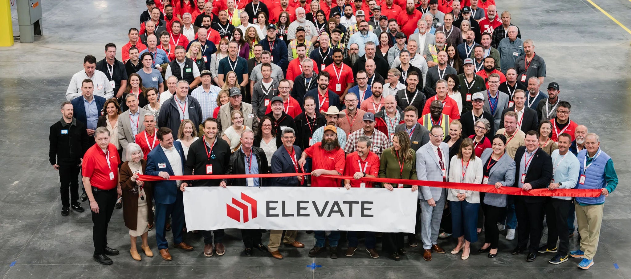  Large group gathered for ribbon-cutting ceremony holding an “Elevate” banner in industrious setting