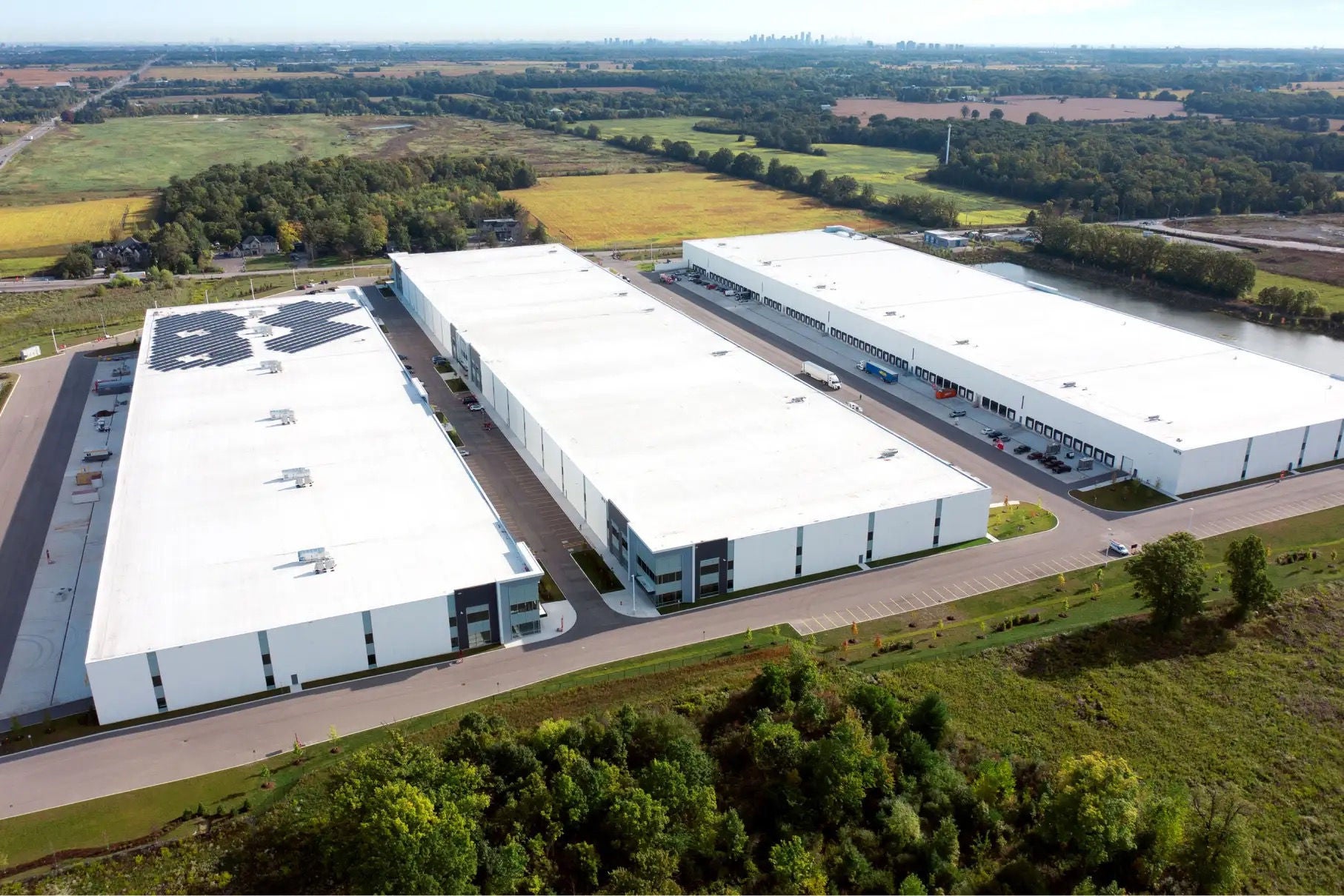 Vue aérienne de trois immenses bâtiments industriels blancs entourés de verdure