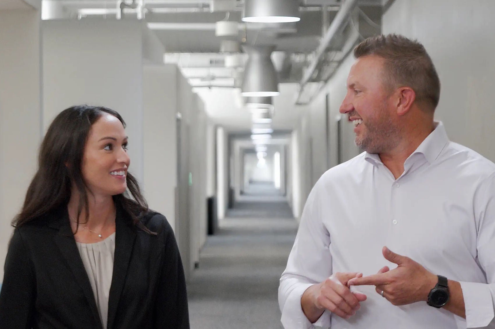 A female worker wearing safety vest, hard hat, and protective eyewear, speaking into a handheld radio at a construction worksite 